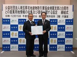 白岡市のバックボードの前で市長と公益社団法人埼玉県宅地建物取引協会埼葛支部の方が一緒に協定書を手に持ち記念撮影している写真