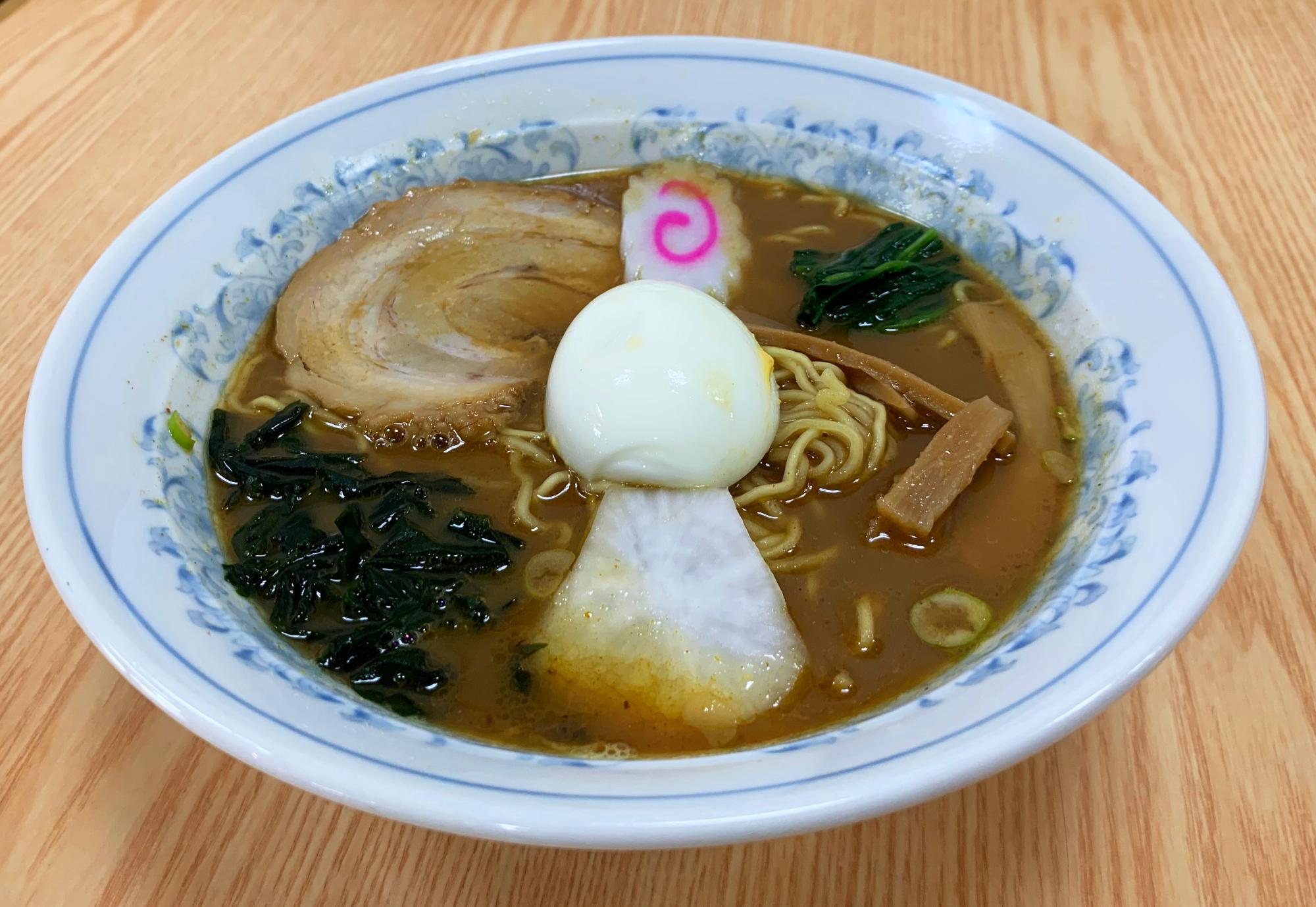 ゆで卵、チャーシュー、ナルト、かぶ、メンマなどのトッピングがのっているシラオカレーラーメンの写真