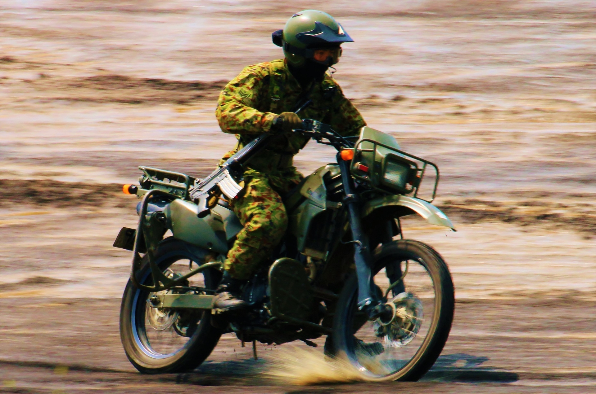 陸上自衛隊の偵察用バイクの写真です。銃を腰に下げた自衛隊員が、悪路をものともせず颯爽と走っています。