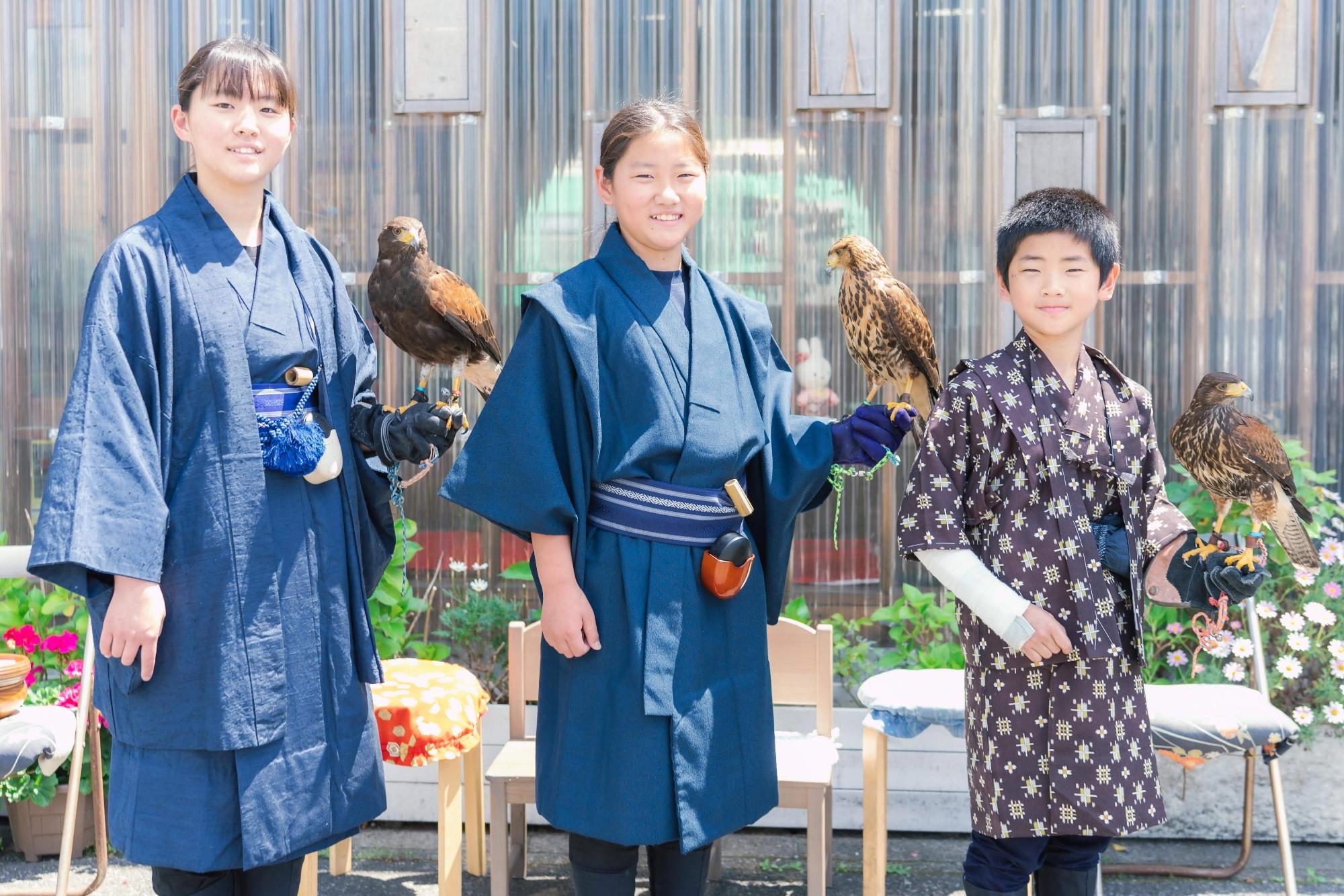 鷹匠体験の様子です。3人のお子さんが腕に鷹を乗せて笑っています。
