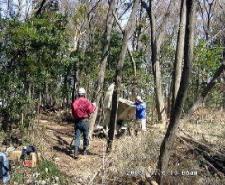 森の中で赤い上着を着ている人と青い上着を着ている人が作業をしている写真