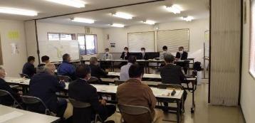 着席している多数の説明会参加者たちと彼らを向いて座っている5人の説明担当者の写真