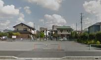 民家の間のフェンスで囲まれている道路沿いの広場の写真