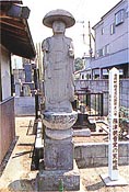 笠をかぶっている石仏の写真。石の土台の上に建てられている。
