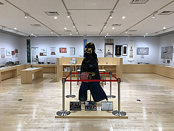 中央に黒い衣装を着たマネキン、奥の壁際にはショーケースに入れられたたくさんの展示品が飾られている歴史資料展示室の写真