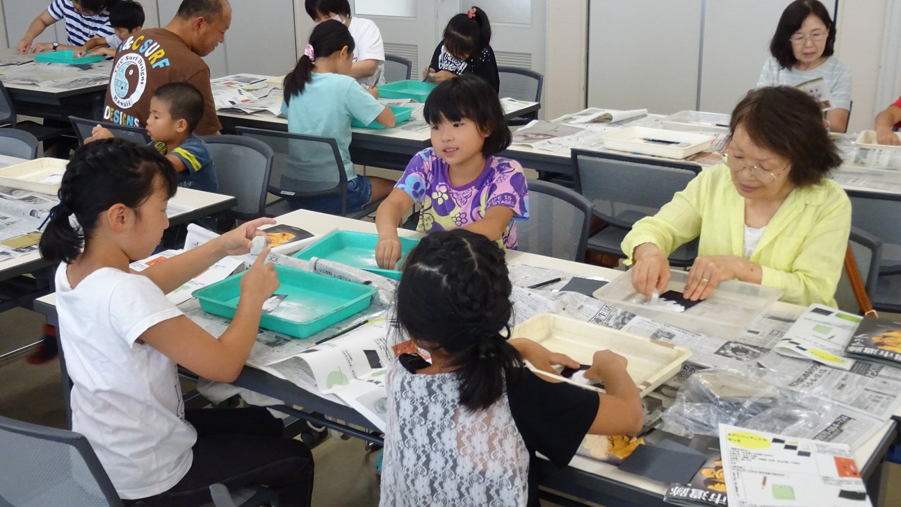 机に広げた新聞紙の上で石をやすりで削る子供たちの写真