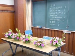 黒板の手前に置かれた机の上に綺麗に飾りつけられた鉢植えが5つ並んでいる写真