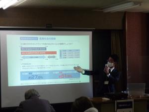 プロジェクターに写し出された資料を指しながらマイクを持って説明をしている男性の講師の方の写真