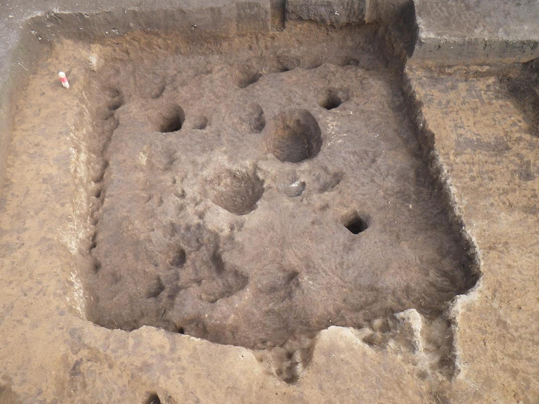 四角形に掘られた溝の中に複数の大きさの違う穴がある発掘された精錬工房跡の写真