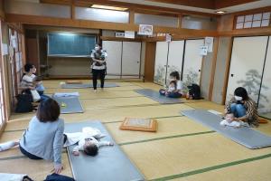 和室で正面に立つ講師の方と、左右に2名ずつ座る親子を部屋の左後方から撮影した写真