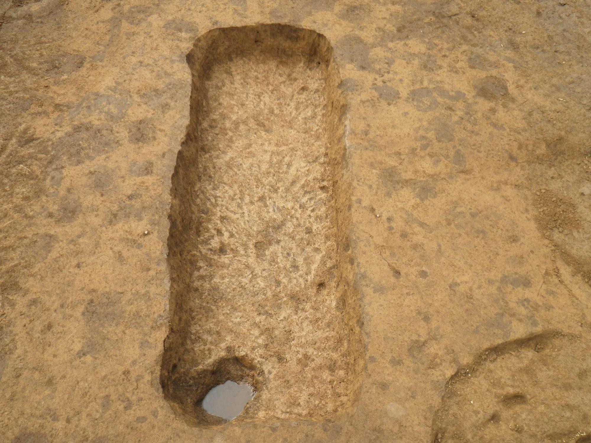 縦に長い四角形の窪んだ穴の左下に円形の小さな穴のある発掘された土坑の写真