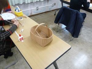 短冊状の素材や接着剤を使って作業をしている女性と、その素材を使って編み込まれたかごの写真