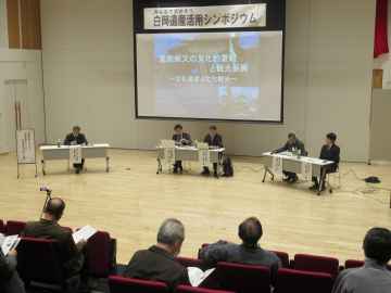 ステージ上に3つの長机に分かれて5人が座り意見交換を行う様子を客席から撮影した写真