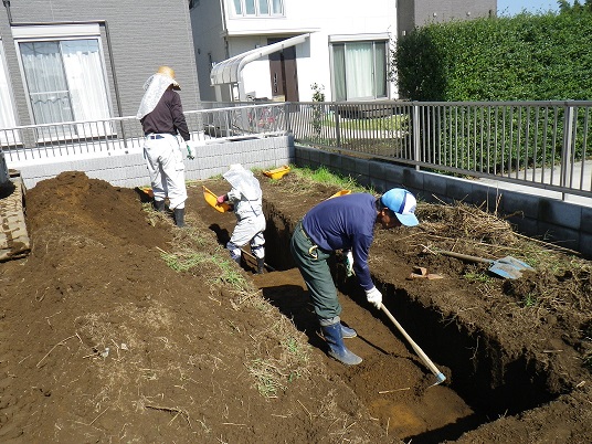 住宅に隣接した土の中を長方形に掘っている作業員の写真