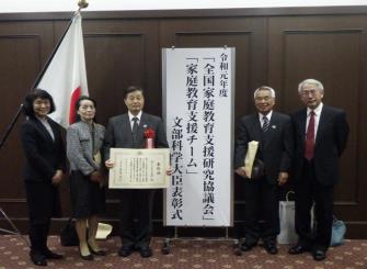 「全国家庭教育支援研究協議会」「家庭教育支援チーム」文部科学大臣表彰式で授与された賞状を手に持ち撮影された「町ぐるみん白岡」の関係者の方の写真
