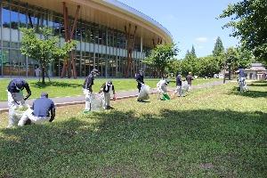 建物横の遊歩道周りの草取りを行っている人達の写真