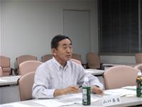 席に座り話をしている様子の山口委員の写真