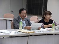 席に座っている男性と女性の参加者が手元の資料を見ている写真