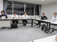 コの字型に設置されたテーブルに参加者たちが座り、会議が行われている様子の写真