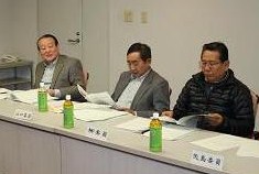 参加者の男性3名が席に着き手元の資料を見ている写真