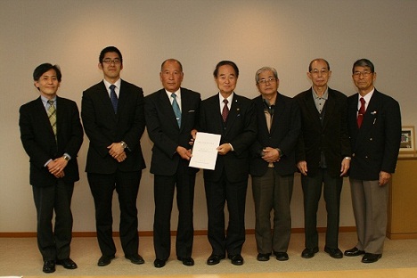 答申書を持った中央の2名と関係者の男性が並び記念撮影をしている写真