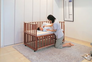 子供部屋でベビーベッドの上の赤ちゃんとその赤ちゃんに布団を掛ける母親の写真