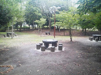 木々の中で石のテーブル三つとそれを囲う石の椅子が移っている写真