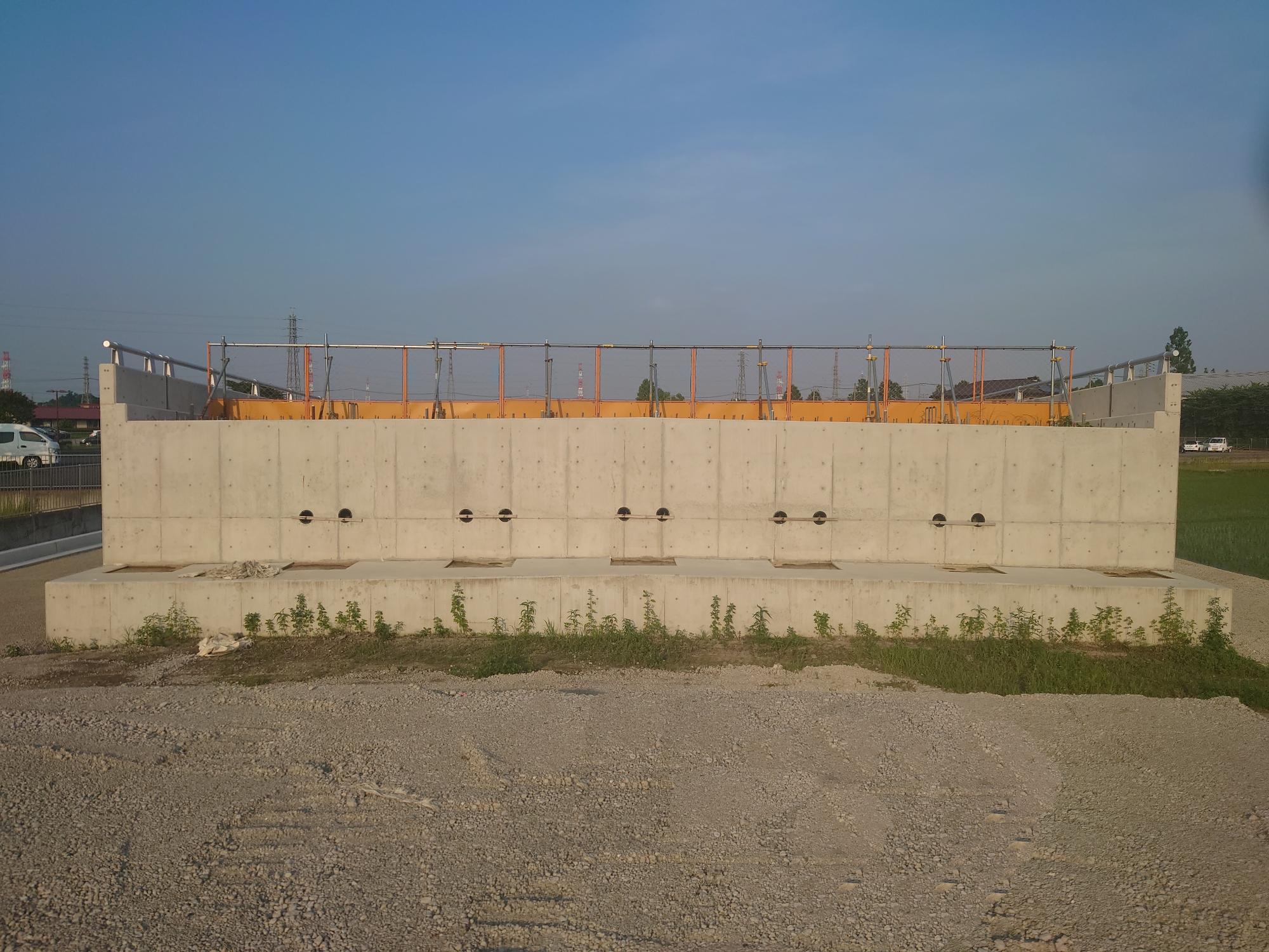 施工中の擁壁部分の上にオレンジ色の工事用のフェンスが並べられている整備中の都市計画道路を正面から撮影した写真