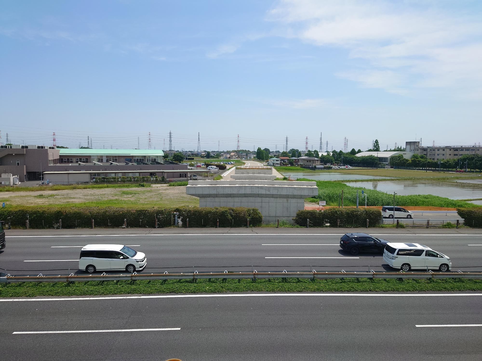 車が行きかう道路の向こう側に白岡宮代線の土台となる橋脚が見える様子を撮影した写真