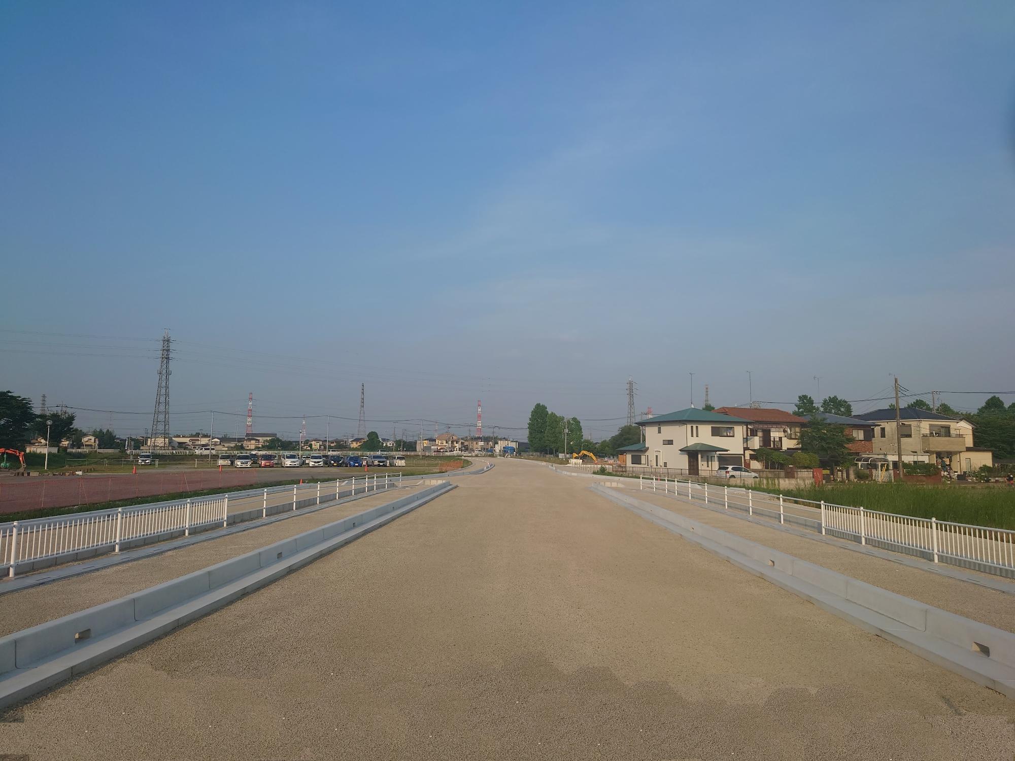 右側に数件の住宅が並び、左側に複数の車が駐車している整備中の都市計画道路の写真