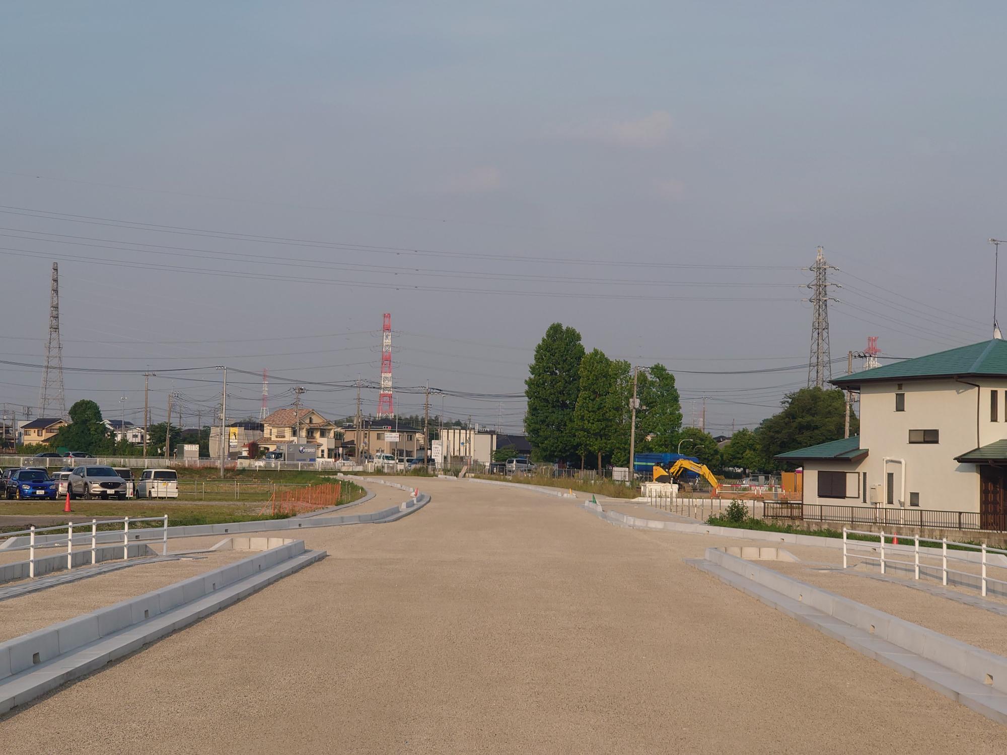 整備中の都市計画道路の左側に複数の車が駐車している様子の写真