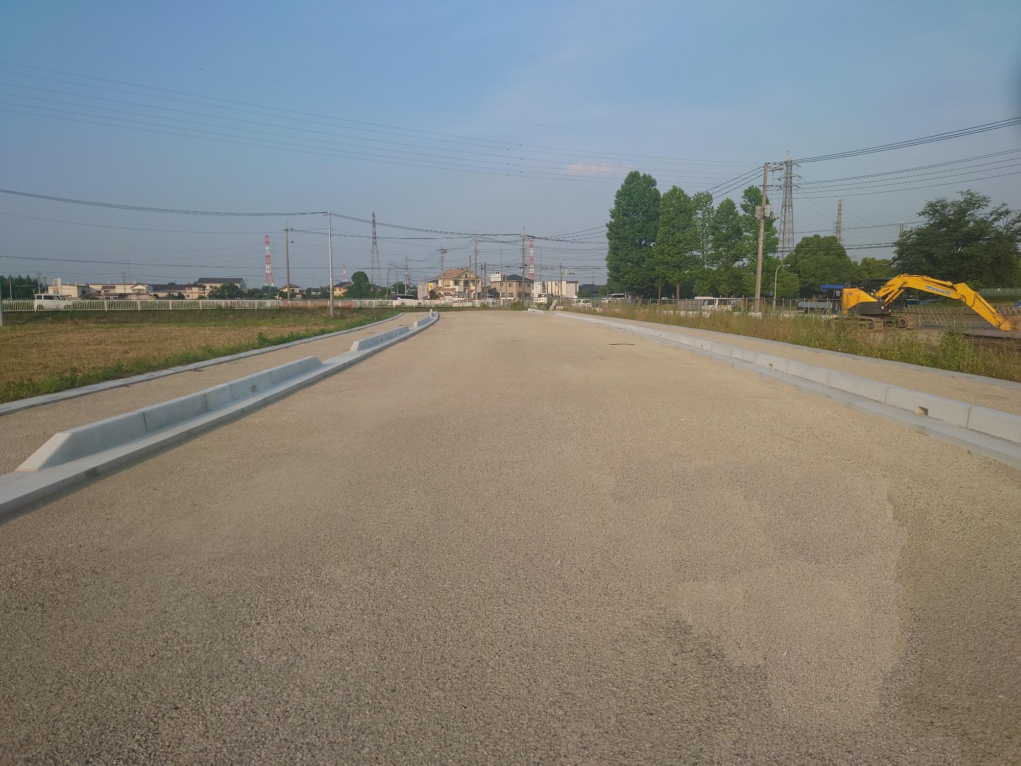 右側に黄色い重機がある都市計画道路の写真