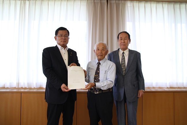 藤井市長と山崎会長が一緒に答申書を持ち、山崎会長の横に大久保副会長が立っている記念撮影している写真