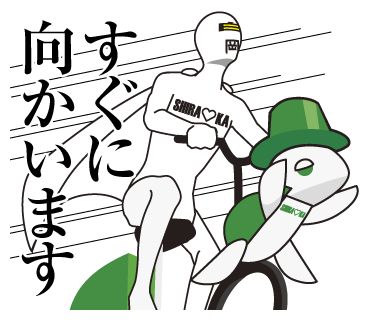 緑の帽子をかぶった白い亀が前についている自転車に乗って走っているシラオ仮面とその左に黒い文字で「すぐに向かいます」と書かれているイラスト