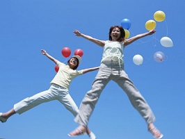 浮かぶ風船と青空を背景に大の字にジャンプする女性二人の写真