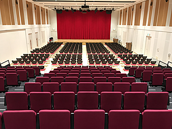 奥に赤い幕が降ろされたステージが見える広い多目的ホールを2階席の一番手前から撮影した写真