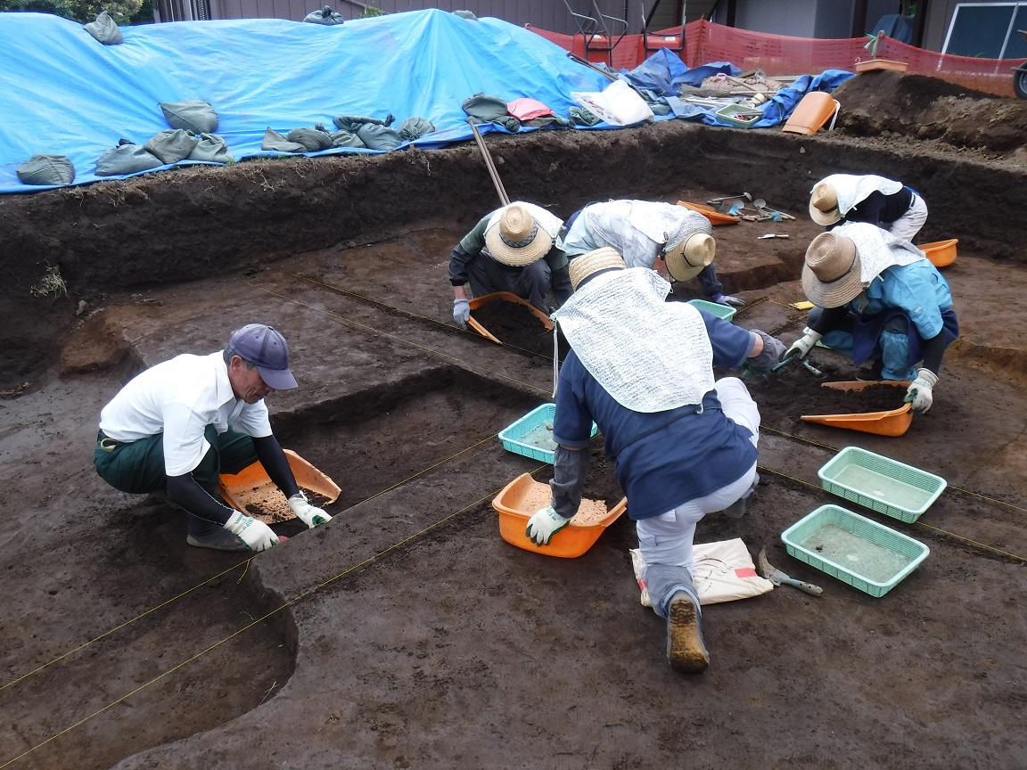 調査区内の地面を掘り確認する作業を行っている6人の作業者の方々の写真