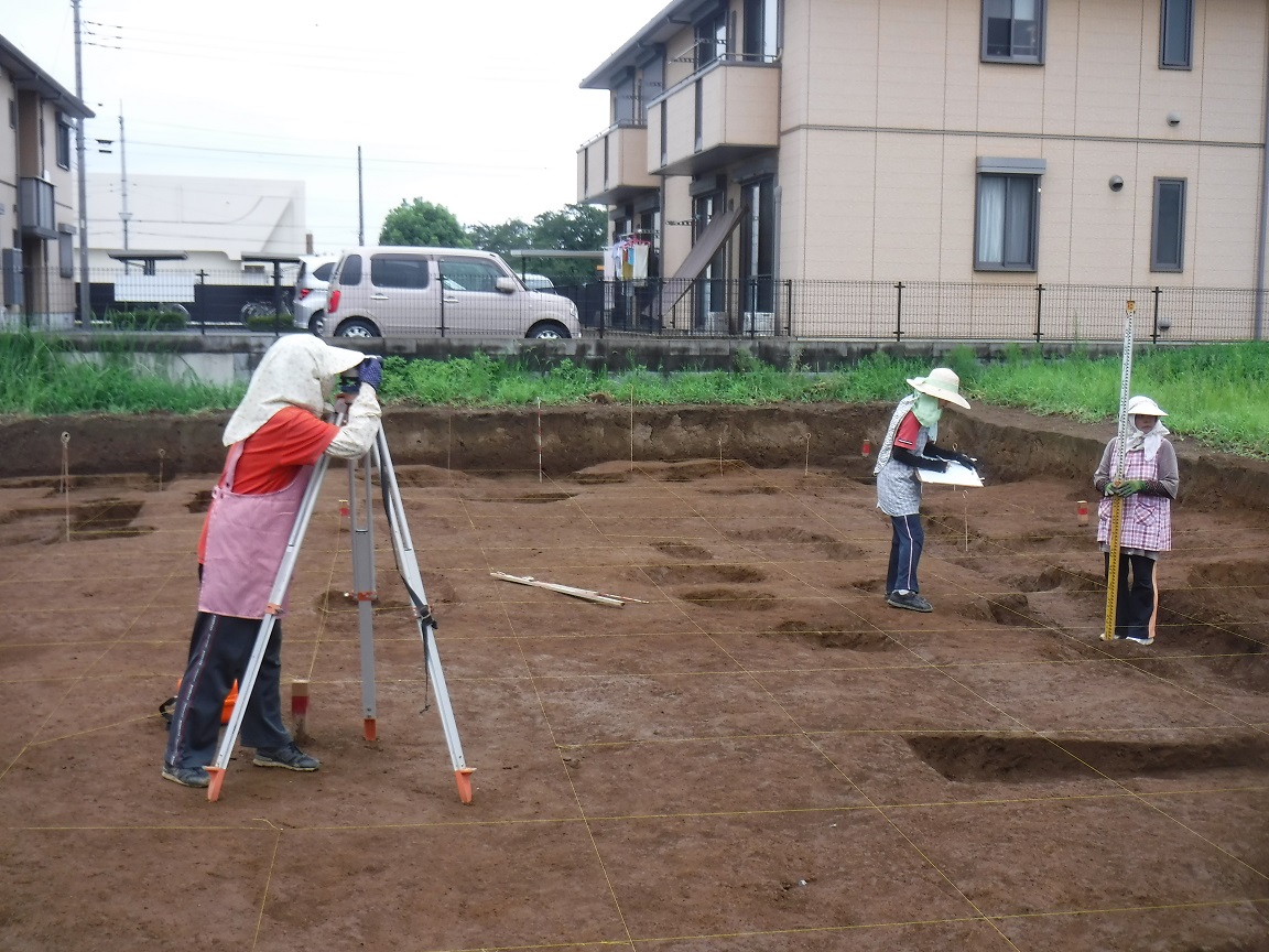 スタッフを持ち立つ女性と測量機をのぞき込む女性と画板を持って書き込む女性の写真