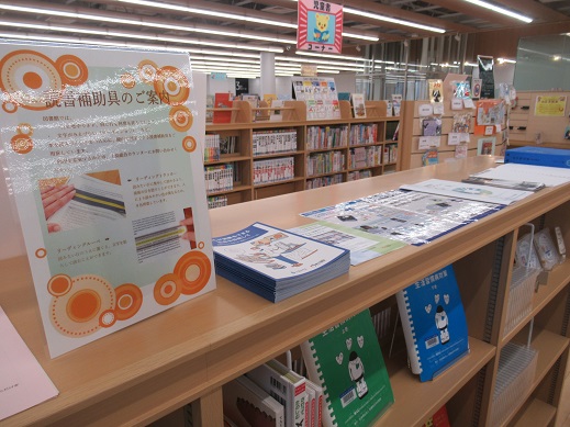 読書補助具のご案内と書かれた補助具の説明が書かれているポップ置かれている本棚の写真