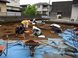 掘った土を手箕に移して出土品を探している作業員と周囲に置かれた一輪車の写真