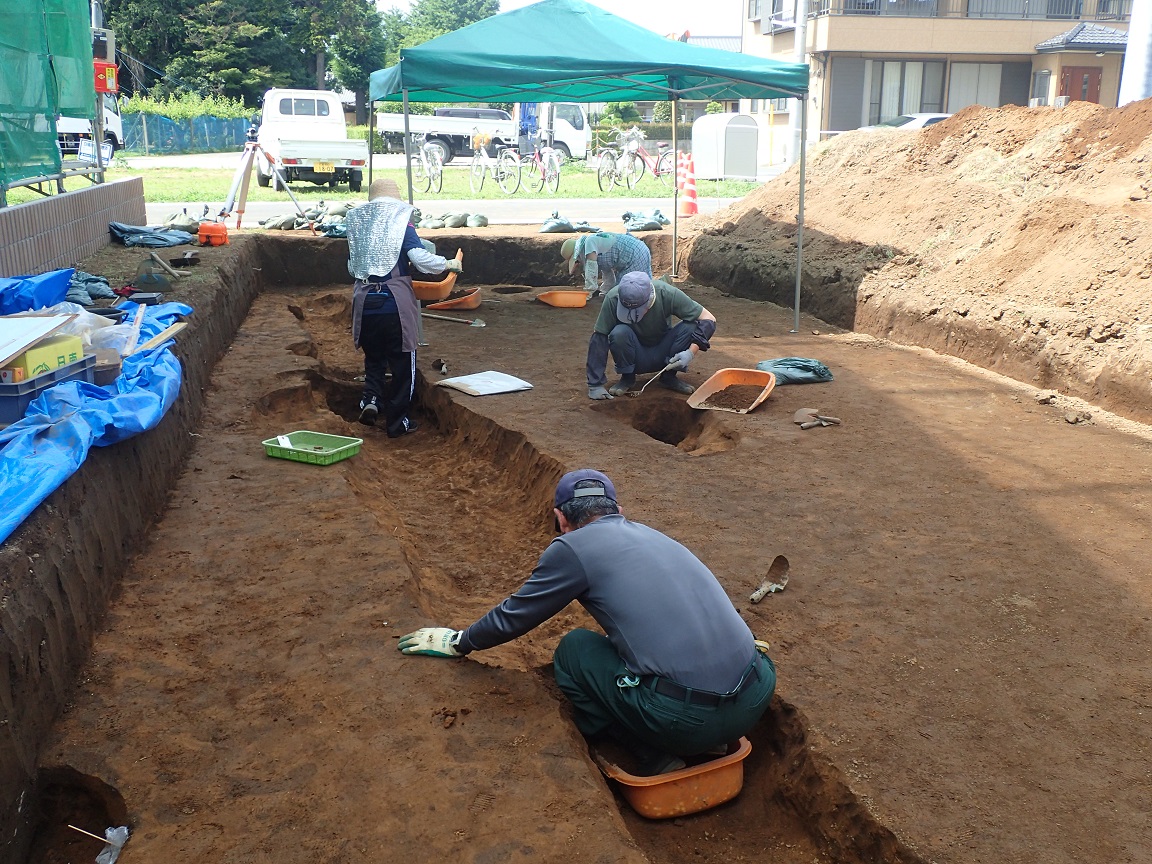 地面に掘られた溝跡や穴の土をスコップで掘って発掘調査をしている作業員の写真