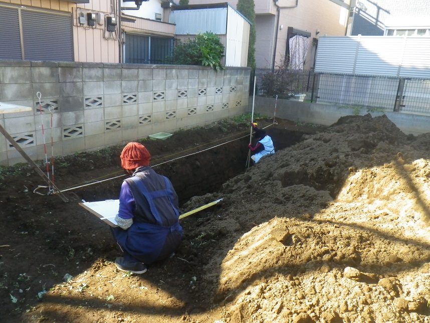 塀の前に深く彫られた穴に入り調査を行っている二人の調査員の方々の写真