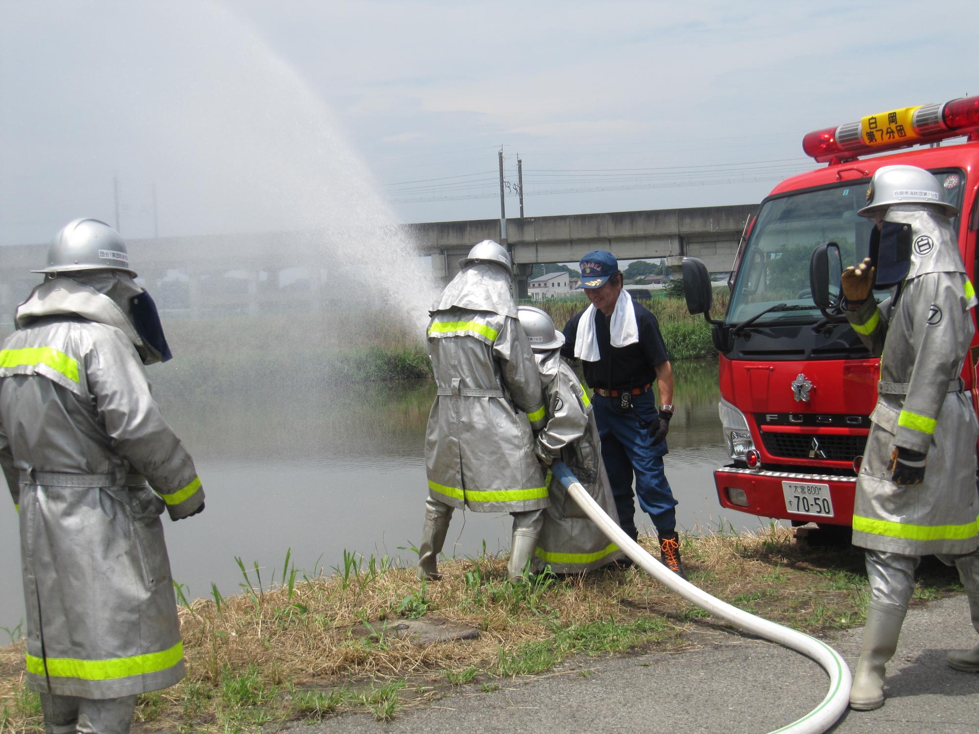 川に向かって放水訓練をする消防隊員の人達の写真